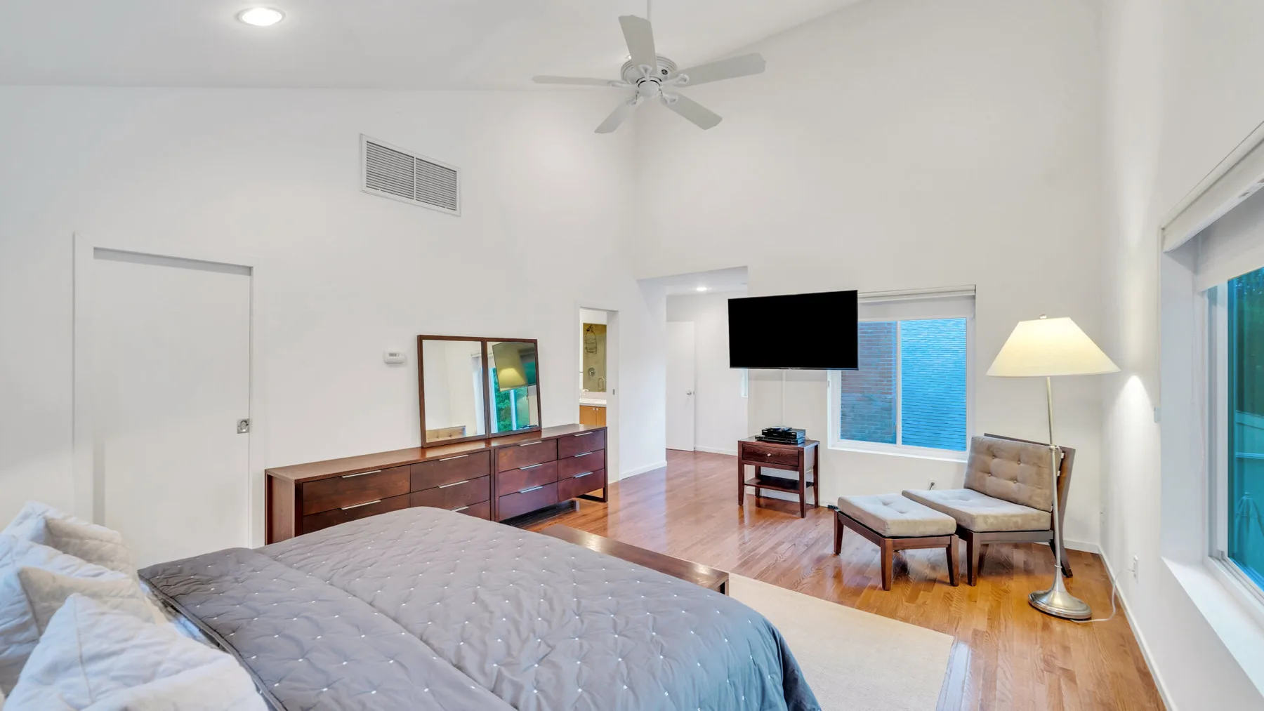 Un dormitorio luminoso con una cama grande, una cómoda de madera y ventanas.