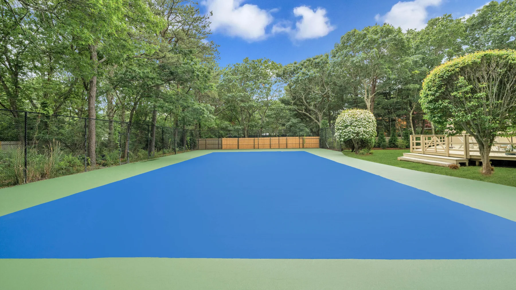Una cancha de tenis azul está rodeada de árboles, con una plataforma de madera al lado.