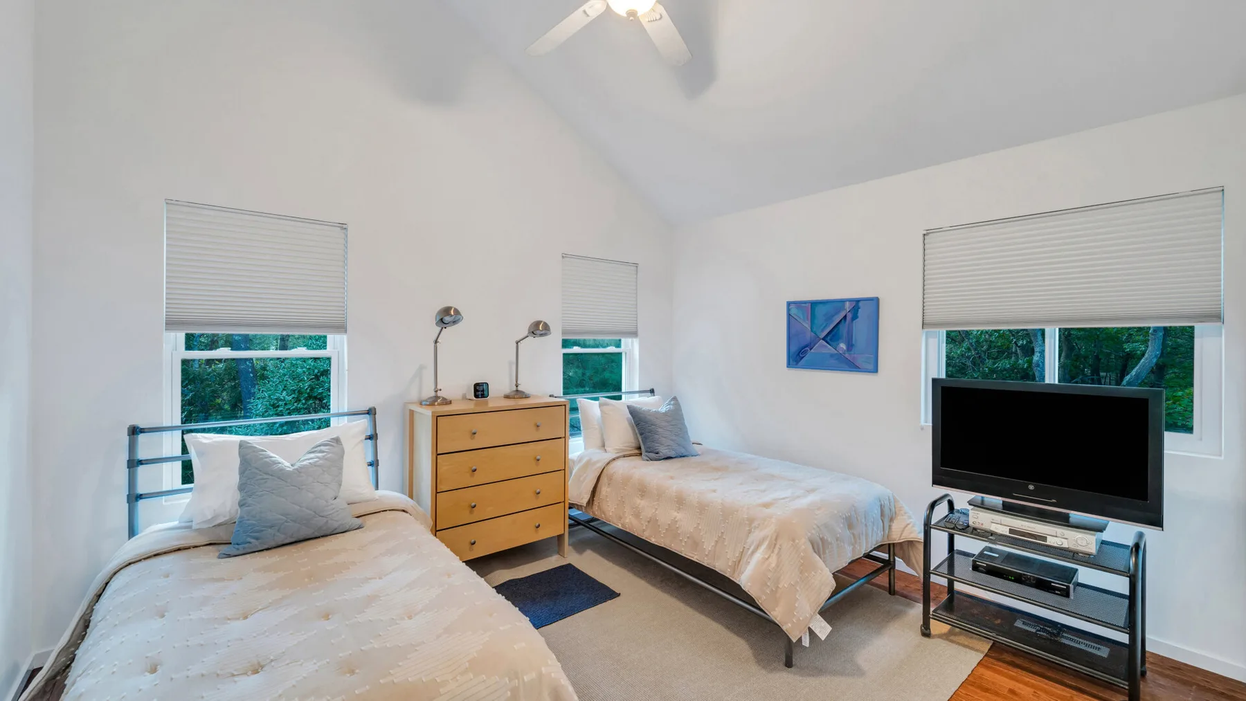 Un dormitorio luminoso con dos camas, una cómoda y un televisor.