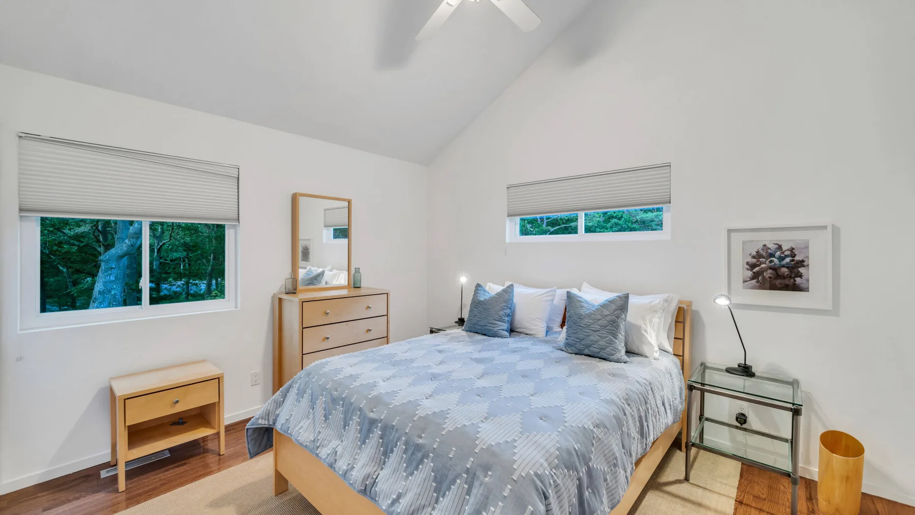 Un dormitorio luminoso con una cama vestida con ropa de cama azul y ventanas con vistas a la vegetación.