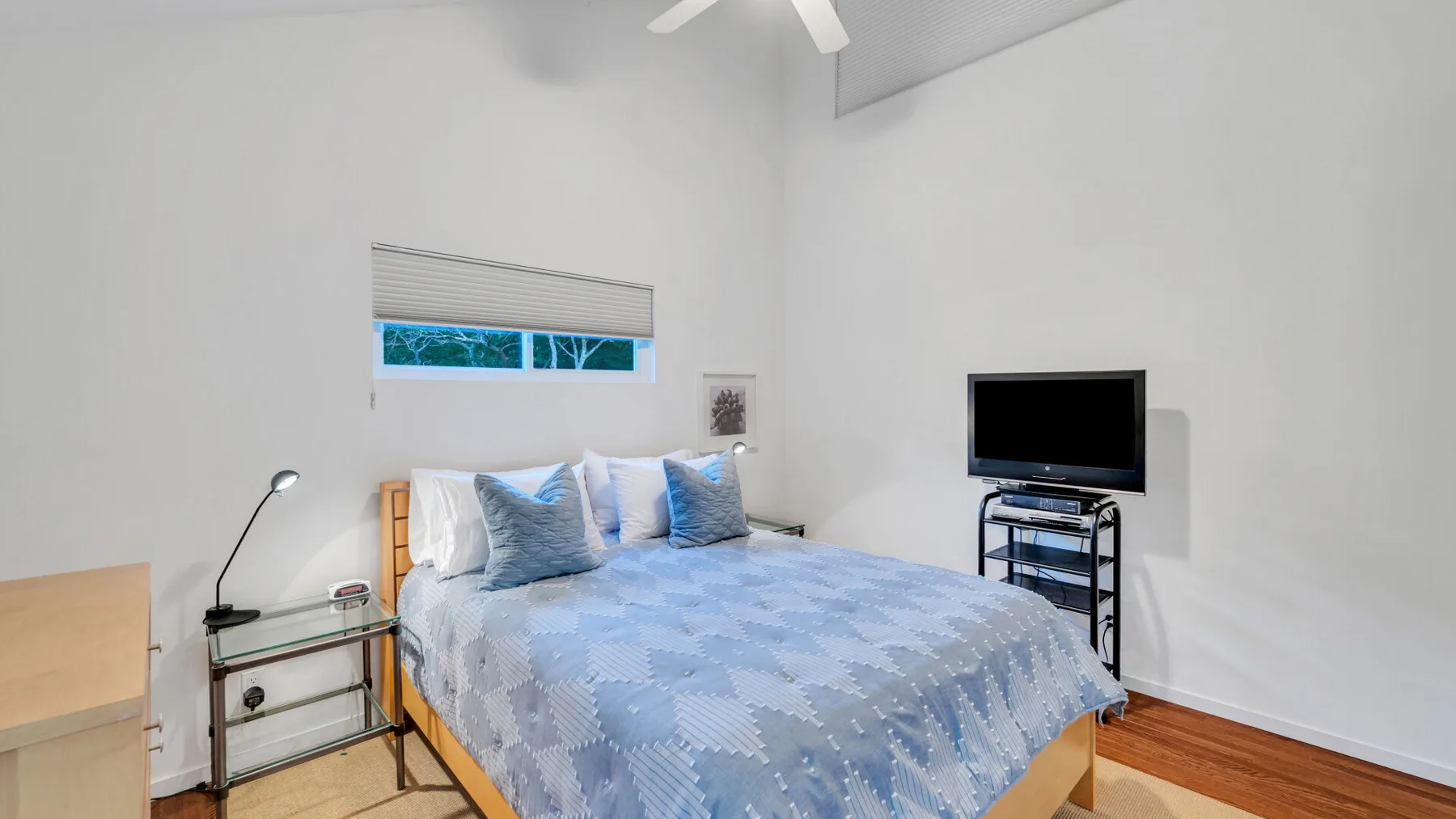 Un dormitorio luminoso con una cama, una mesita de noche y un televisor.