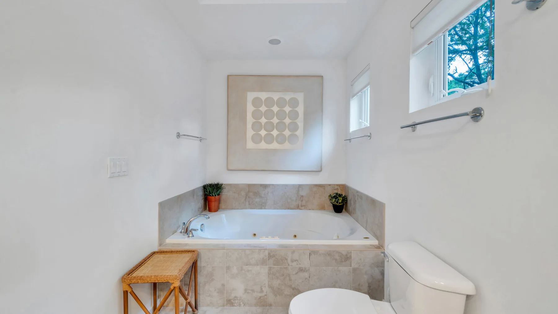 Un baño luminoso con una bañera empotrada y un cuadro geométrico enmarcado.