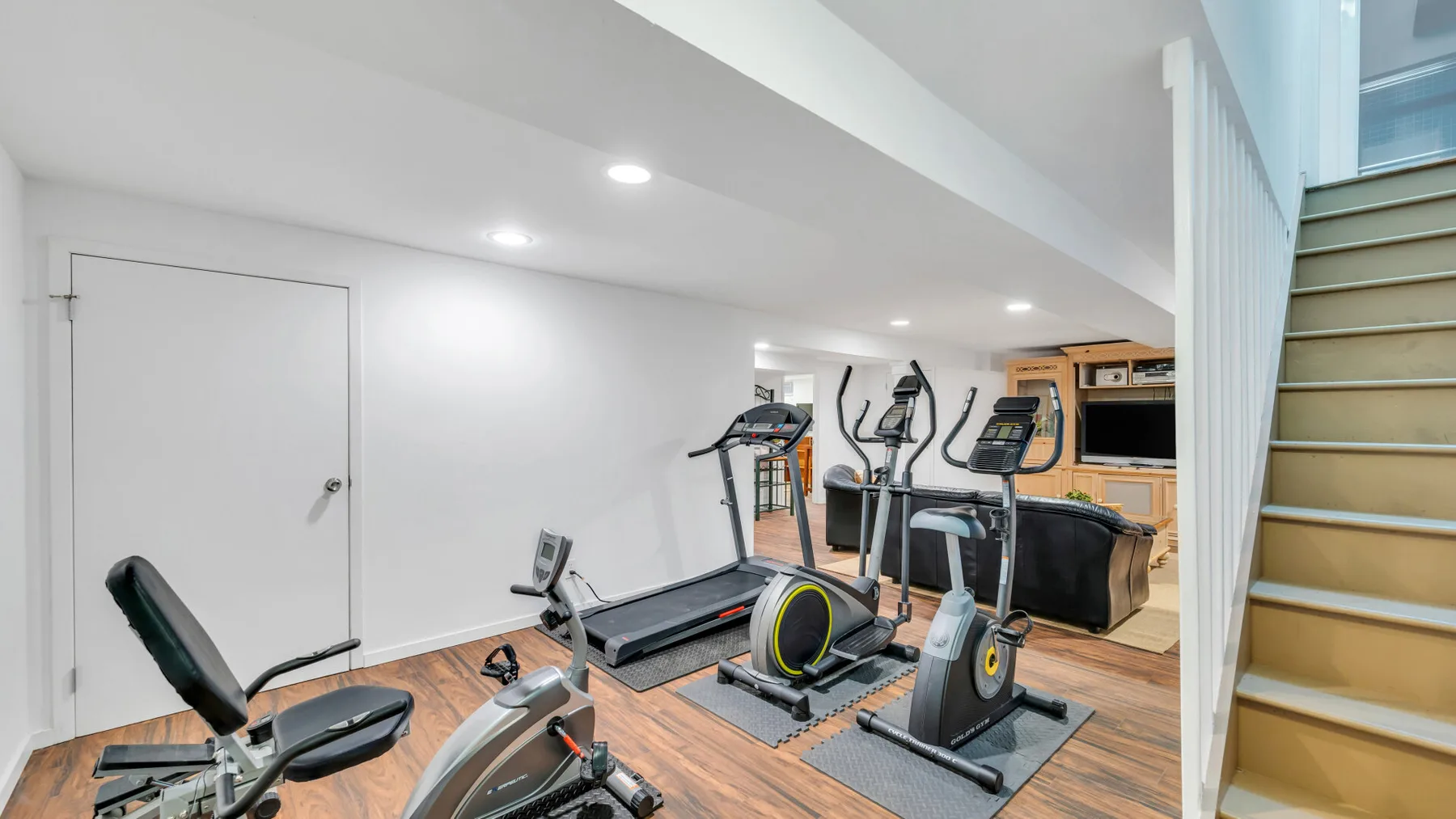 Un gimnasio en casa con máquinas de ejercicio y una escalera a la derecha.