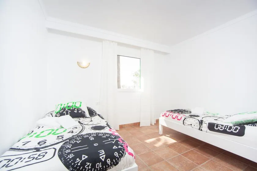 A bright bedroom with two beds and a small window.