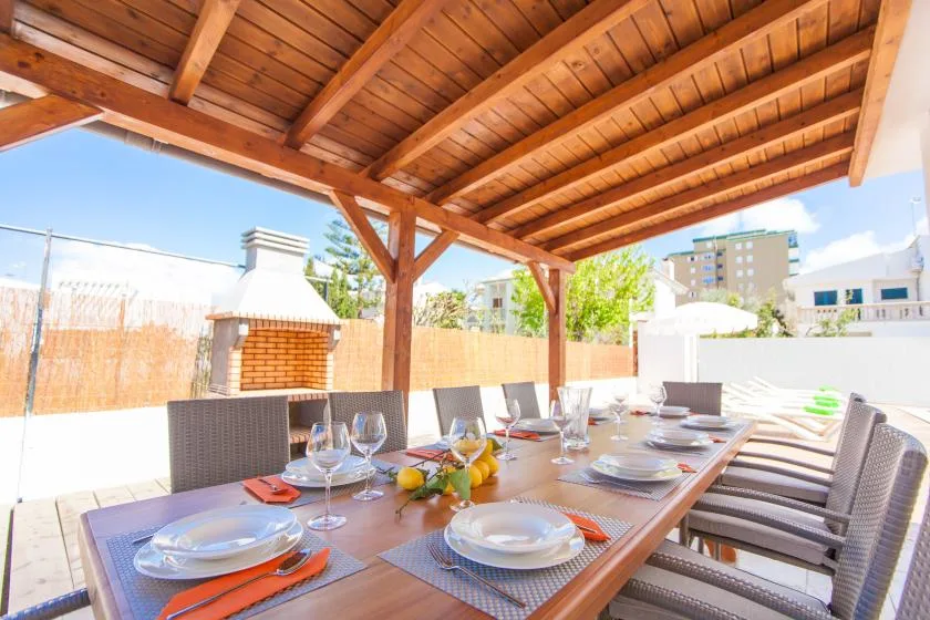 A covered outdoor dining area has a long table set with dishes and glassware.