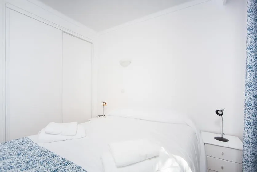 A bright bedroom with white bedding and a blue patterned curtain.