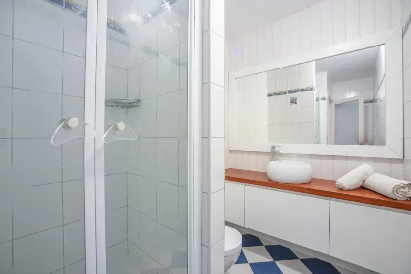 A tiled bathroom with a glass shower and a long vanity beneath a mirror.