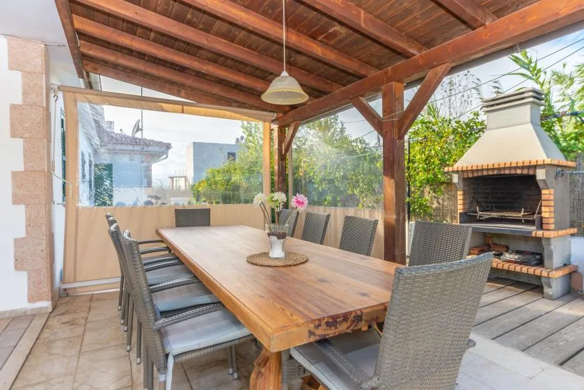 A covered outdoor dining area with a long table and built-in barbecue.
