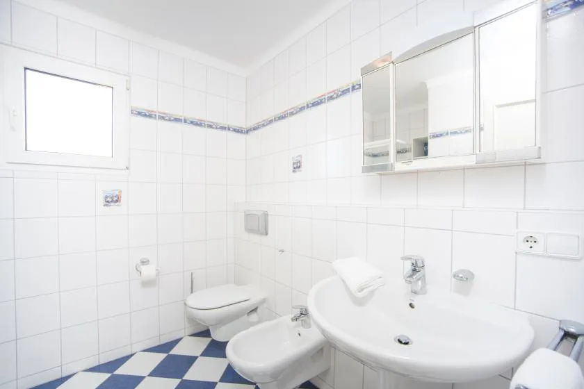 A bright tiled bathroom with a bathtub, sink, and mirrored cabinet.