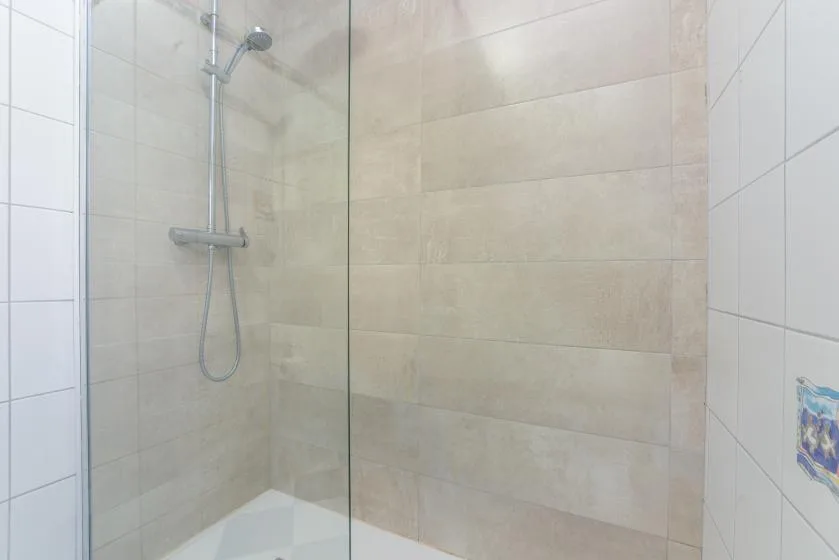 A tiled shower with a wall-mounted showerhead and glass panel.