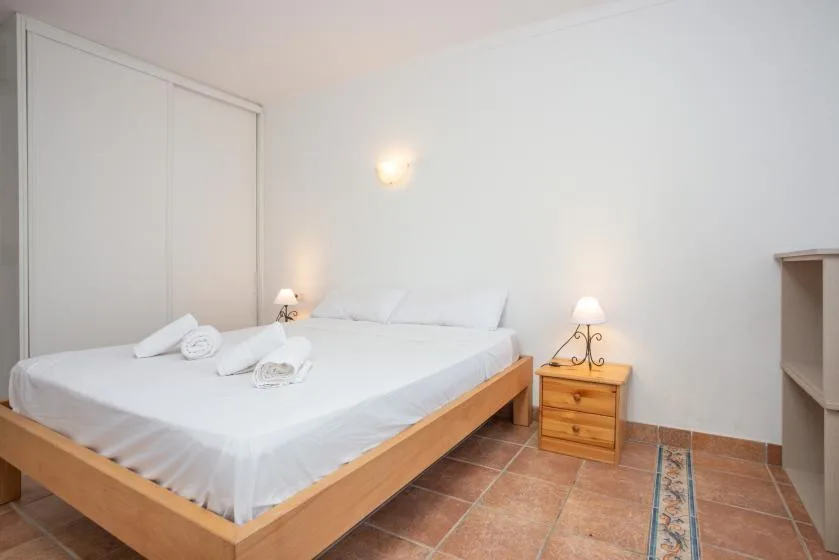 A bedroom with a bed, bedside table, and tiled floor.
