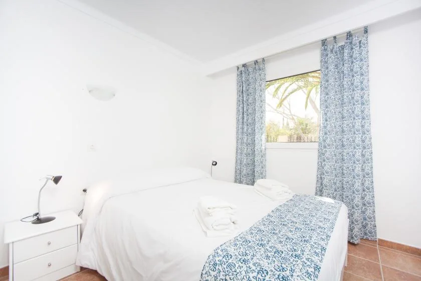 A bedroom with white bedding and patterned curtains beside a window.