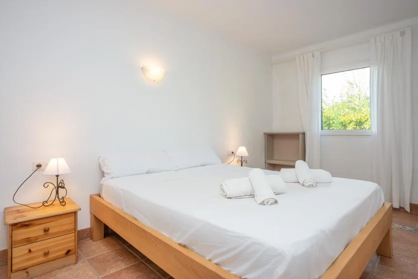 A bright bedroom with a large bed, bedside tables, and a window.