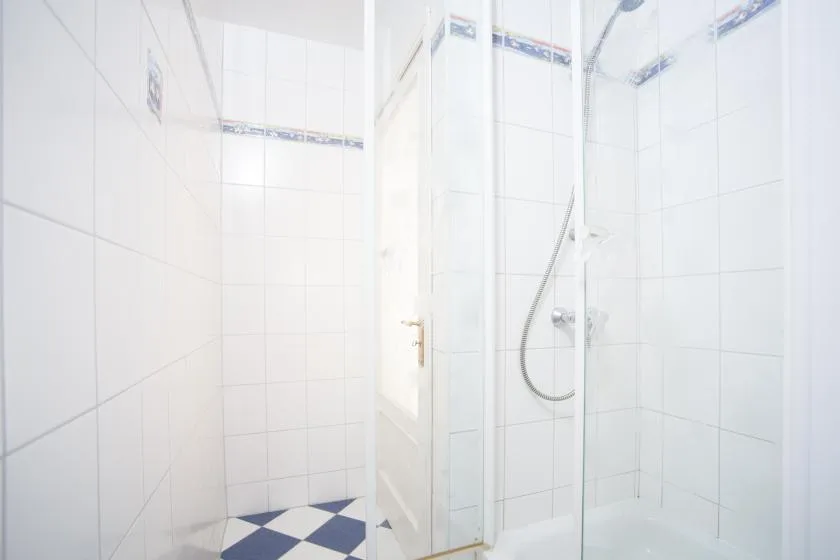 A tiled bathroom with a glass shower enclosure and handheld showerhead.