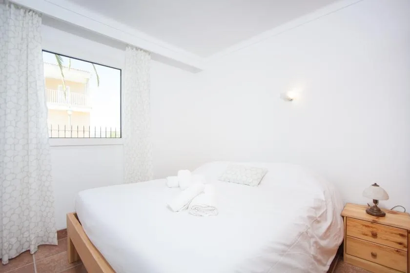 A bright bedroom with a white bed beside a window and wooden nightstand.
