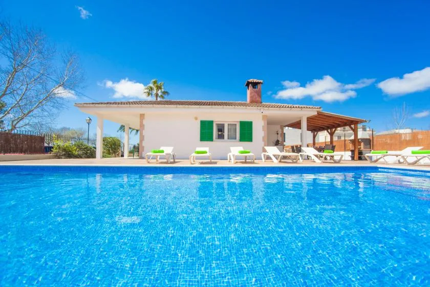 A swimming pool sits in front of a house with a covered patio.