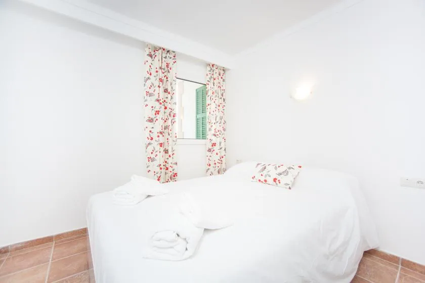A bright bedroom with white bedding and floral curtains beside the bed.