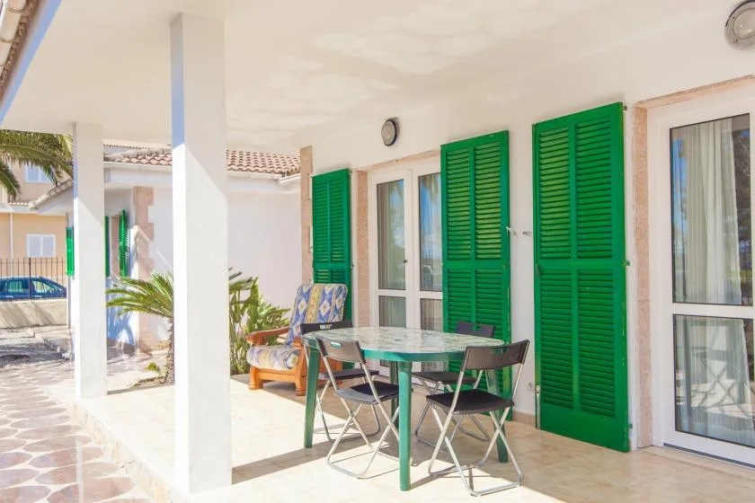A covered patio with a dining table and green shutters along the wall.