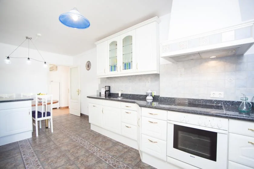 A bright kitchen with white cabinets, a long countertop, and a dining table.