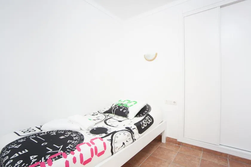 A single bed with patterned bedding sits in a bright white room.
