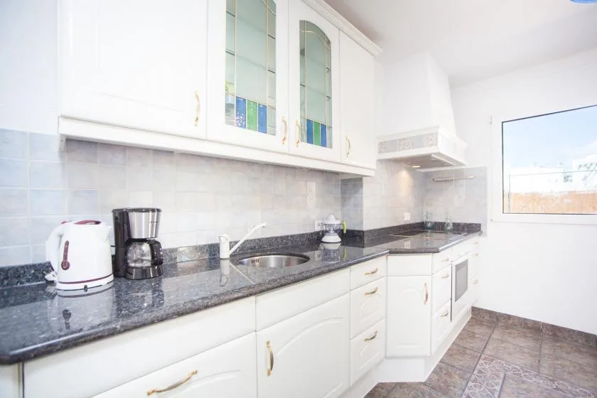 A bright kitchen with white cabinets, dark countertops, and a window.