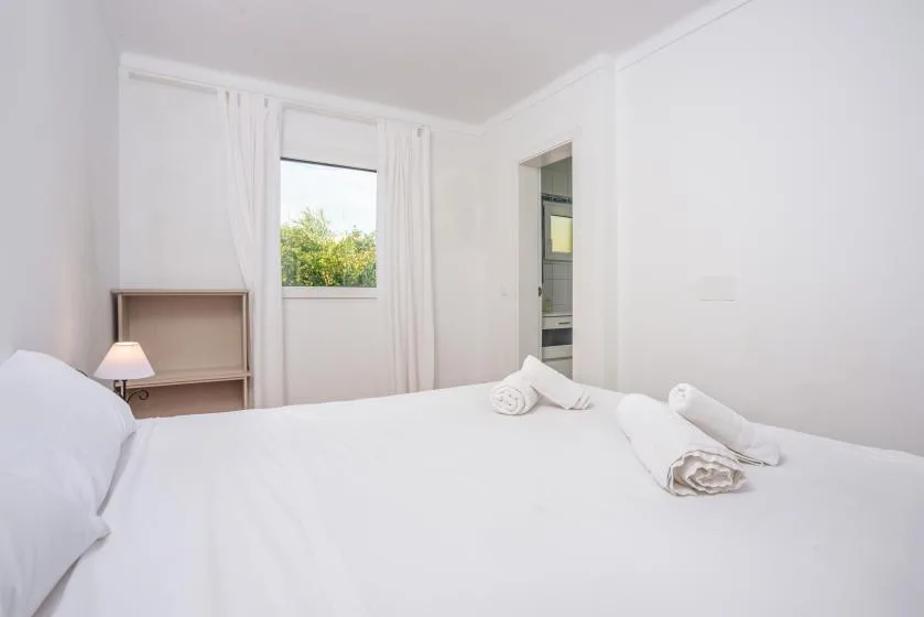 A bright bedroom with a large bed and a window framed by curtains.