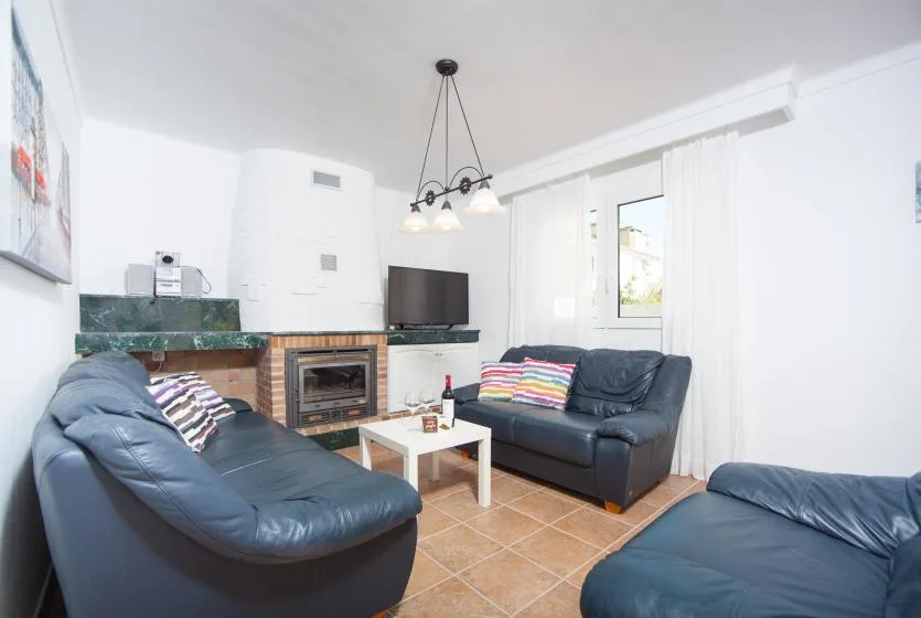 A bright living room with dark seating arranged around a television and fireplace.