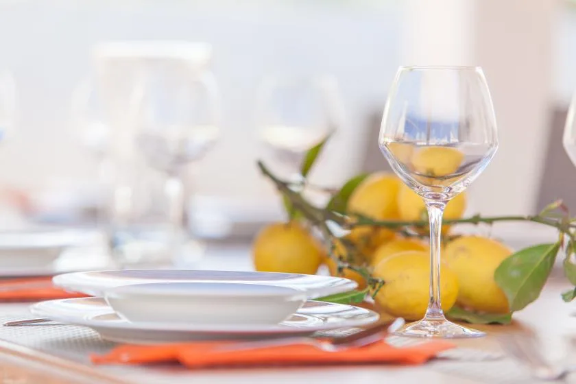 A dining table is set with plates, wine glasses, and fresh lemons.