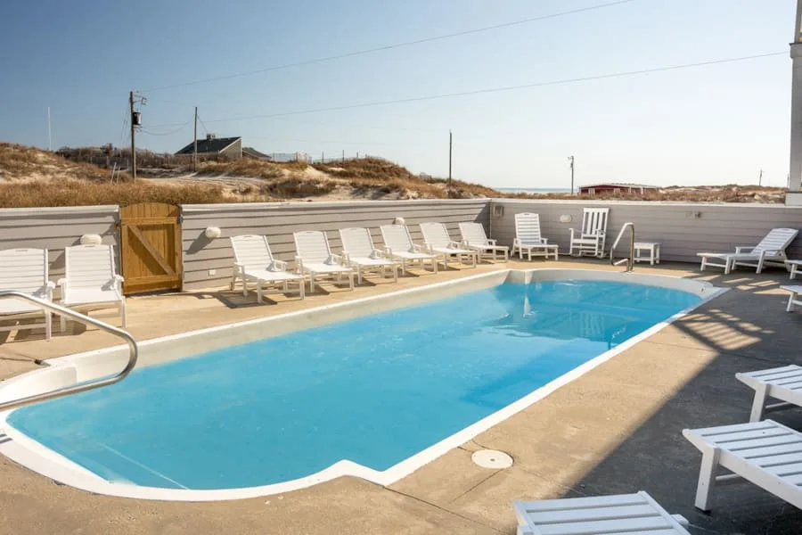 An outdoor swimming pool is surrounded by lounge chairs on a sunny day.