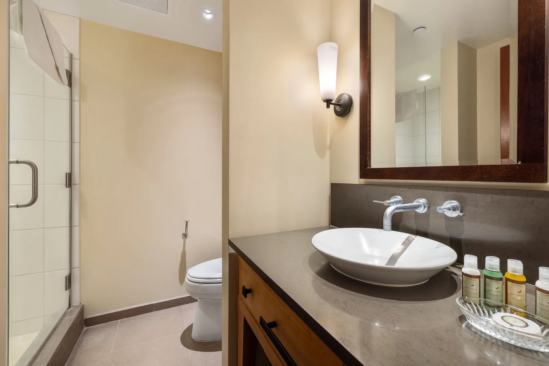 Un tocador de baño con lavabo sobre encimera, espejo y ducha a un lado.