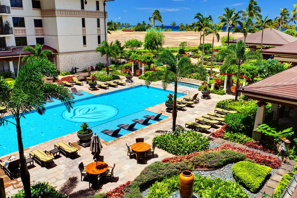 Una zona de piscina al aire libre ajardinada, con asientos y palmeras alrededor.