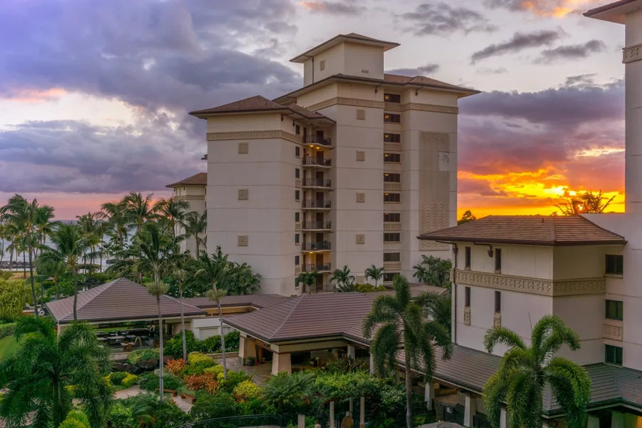 Un edificio turístico se alza sobre jardines ajardinados bajo un cielo de atardecer colorido.