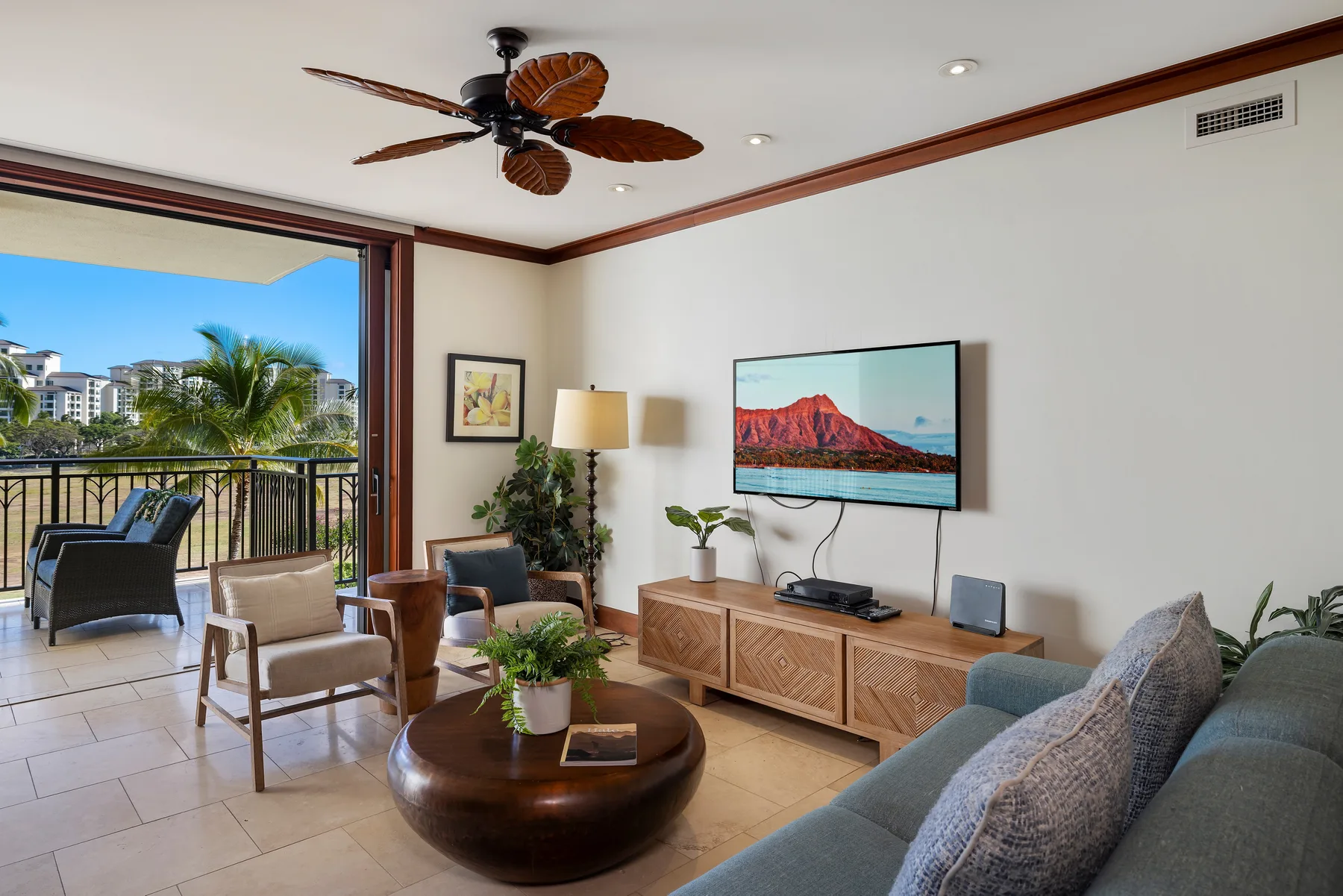 Una sala de estar con asientos, un televisor y un balcón abierto.