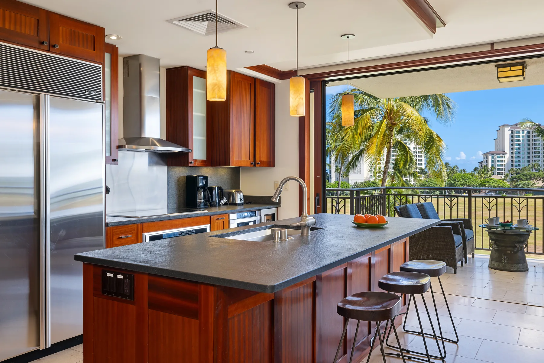 Una cocina moderna se abre a un balcón con palmeras y edificios de la ciudad.