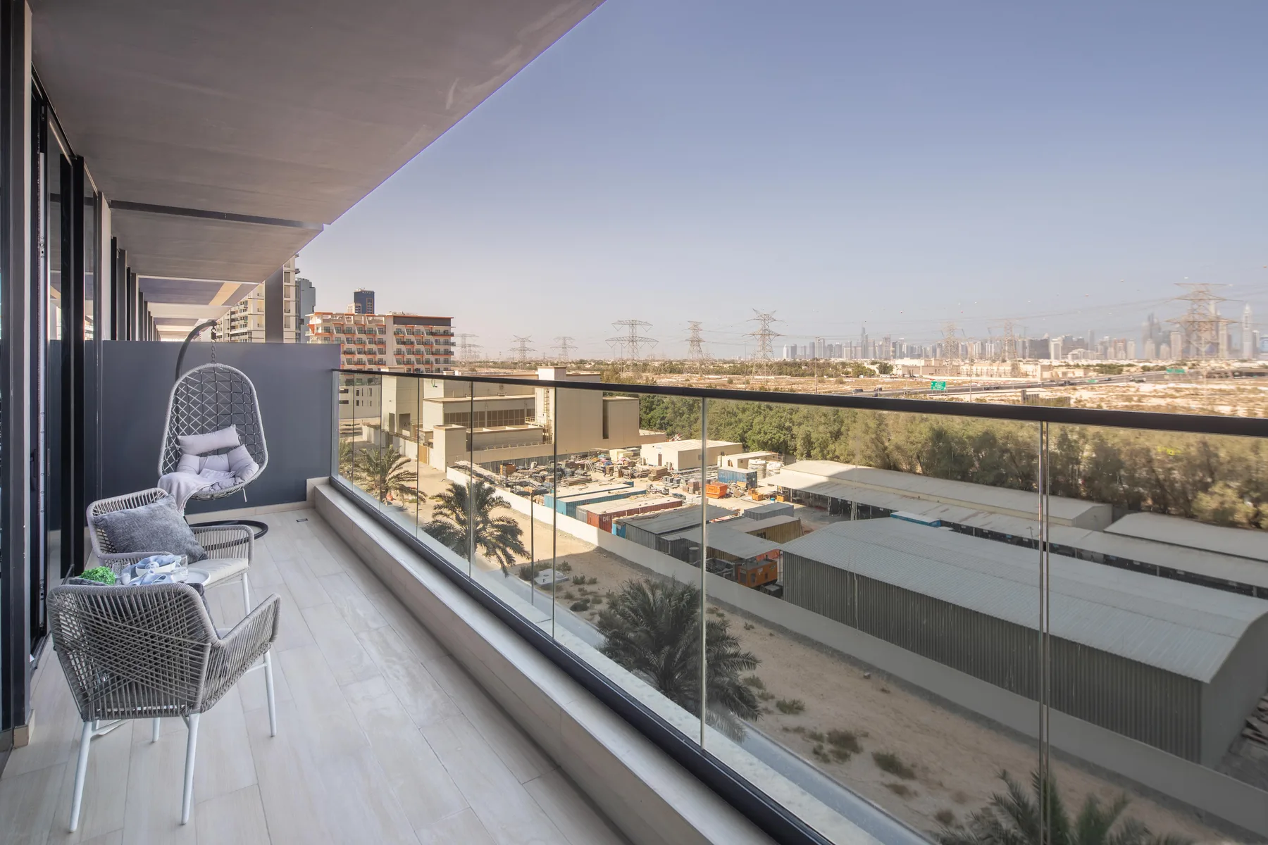 A balcony with seating overlooks nearby buildings and a distant city skyline.
