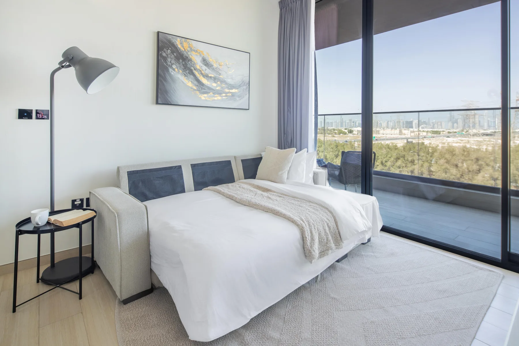 Un dormitorio luminoso con una cama blanca junto a grandes ventanales con vistas al paisaje.