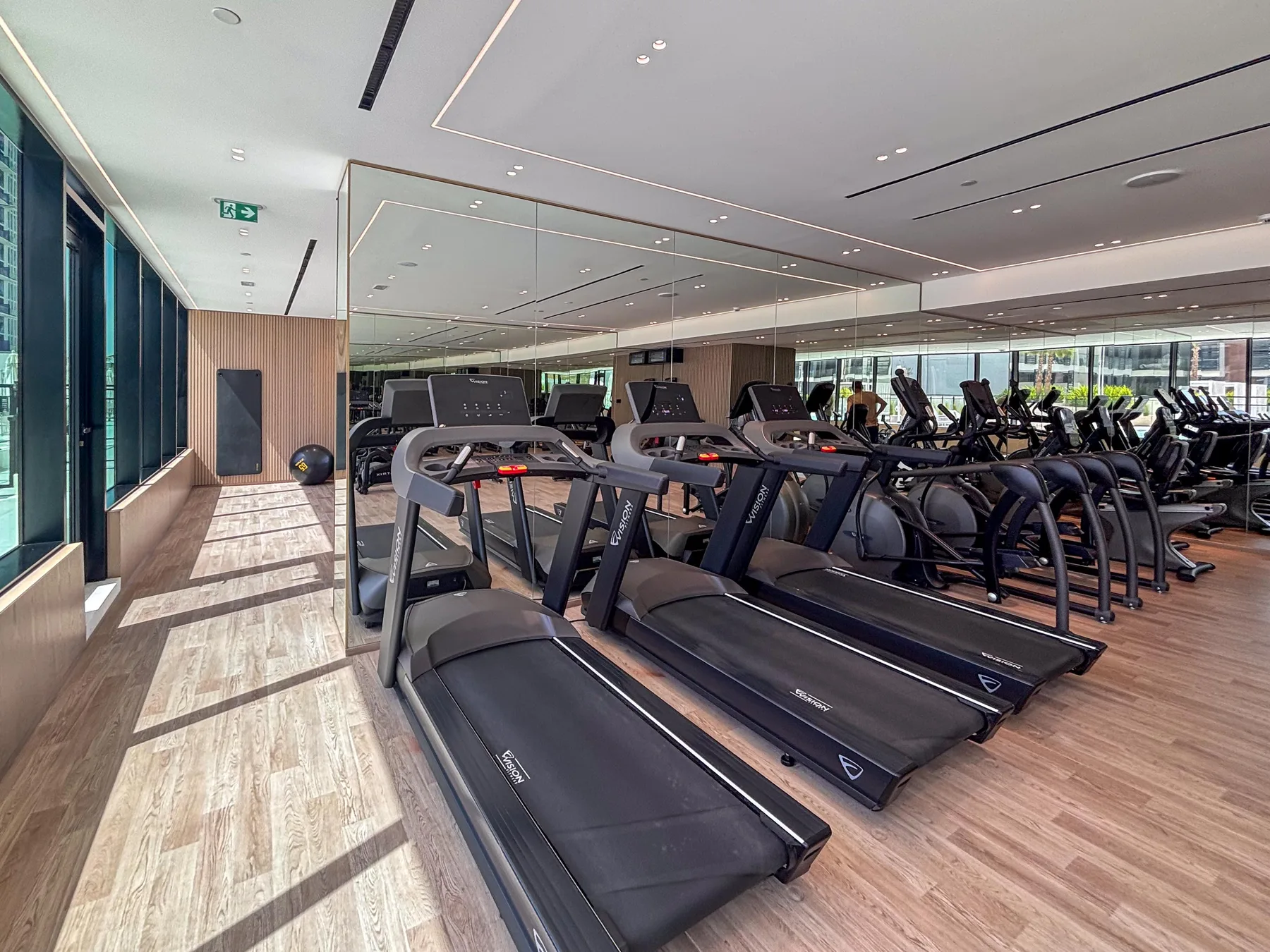 A gym with rows of treadmills and exercise machines beside large windows.