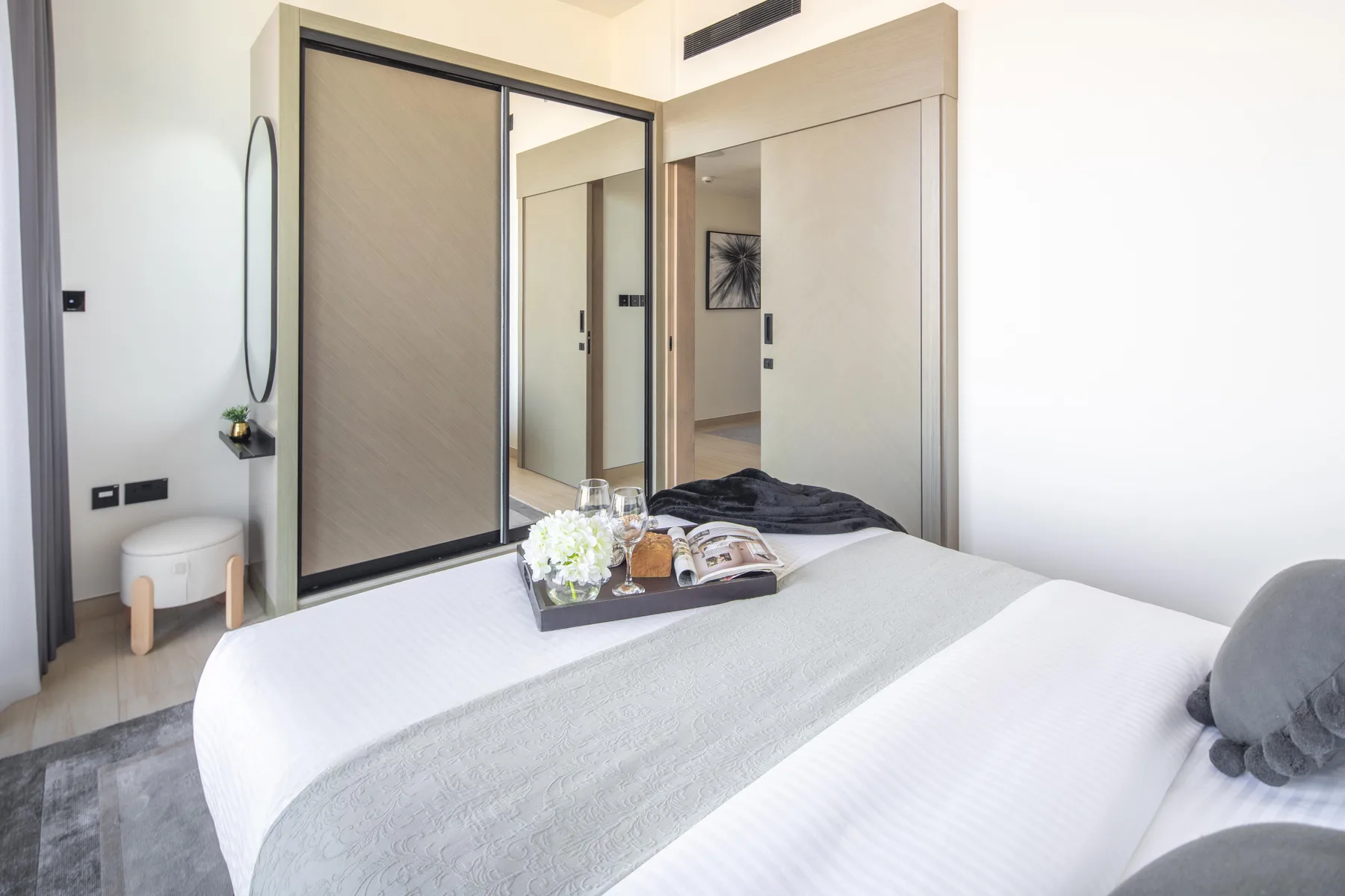 A bright bedroom with a neatly made bed and mirrored wardrobe.