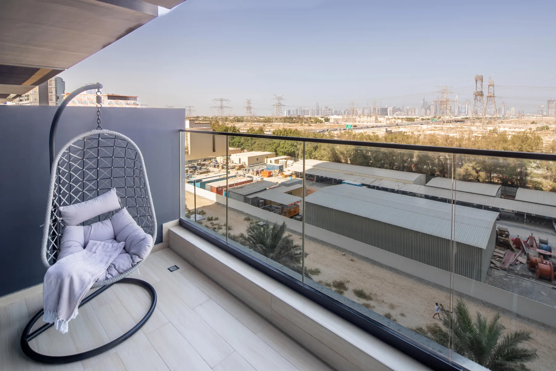 A balcony with a hanging seat overlooks low buildings and a distant cityscape.