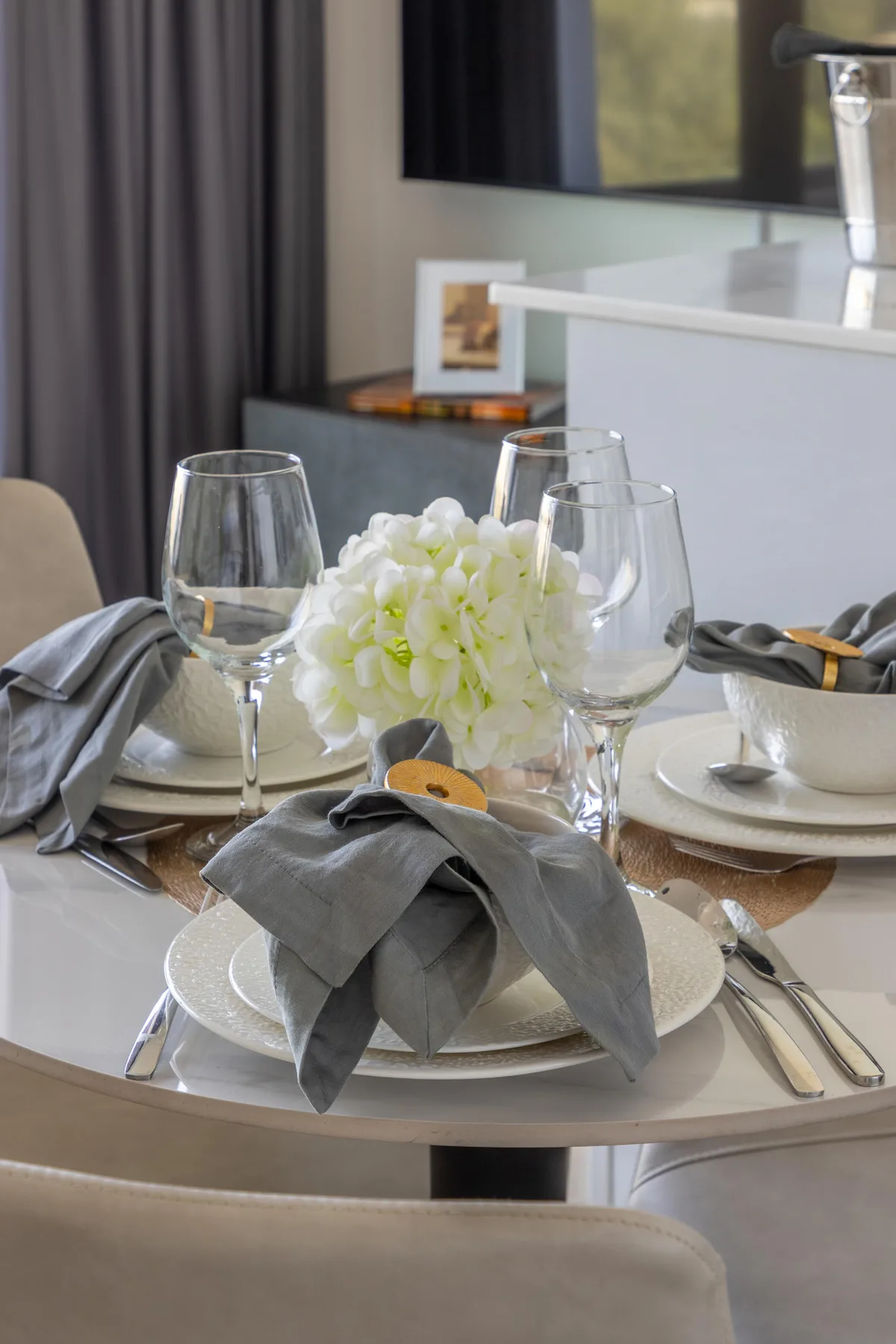 A dining table is set with plates, glassware, folded napkins, and a floral centerpiece.