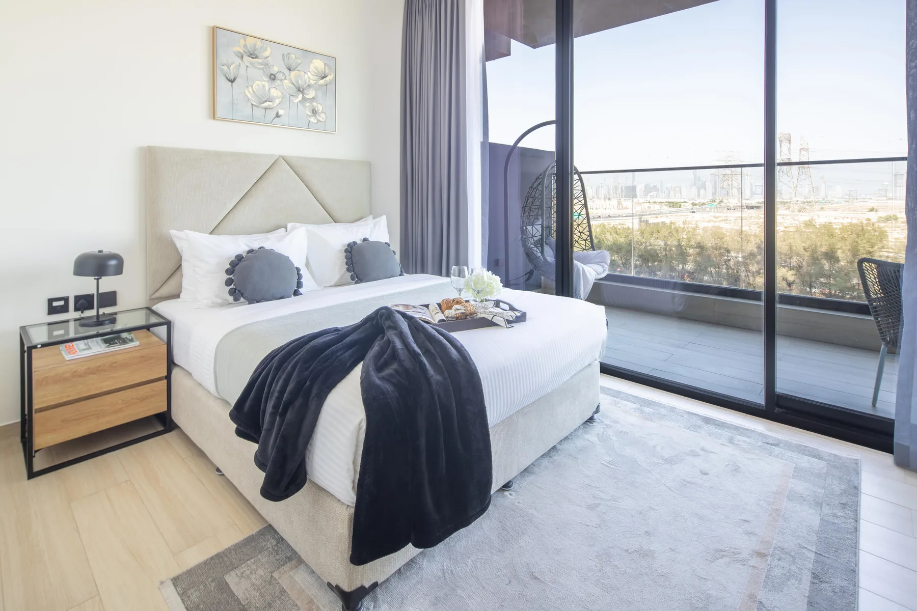 A bright bedroom with a neatly made bed beside floor-to-ceiling windows.