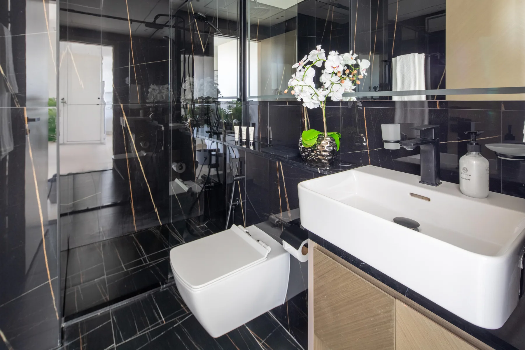 A modern bathroom with a white sink, toilet, and dark tiled walls.
