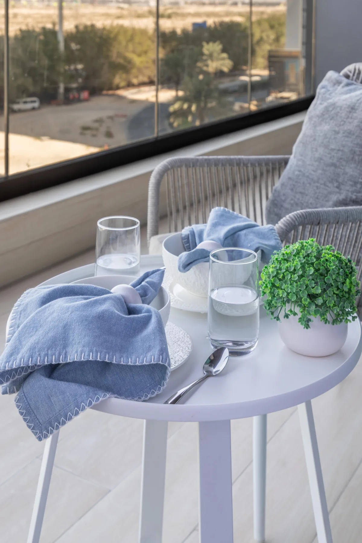 A small table with folded towels and glasses beside a window overlooking greenery.