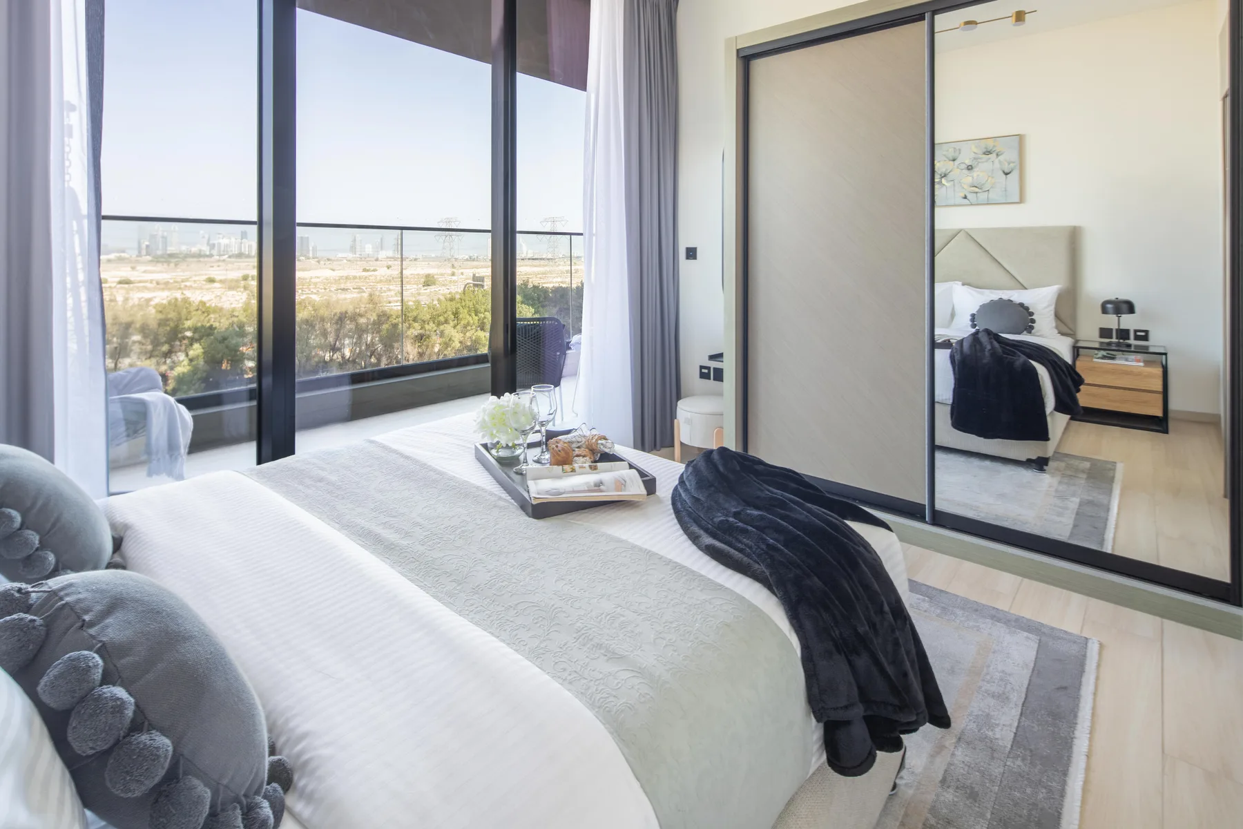 A bright bedroom with a large bed beside floor-to-ceiling windows.