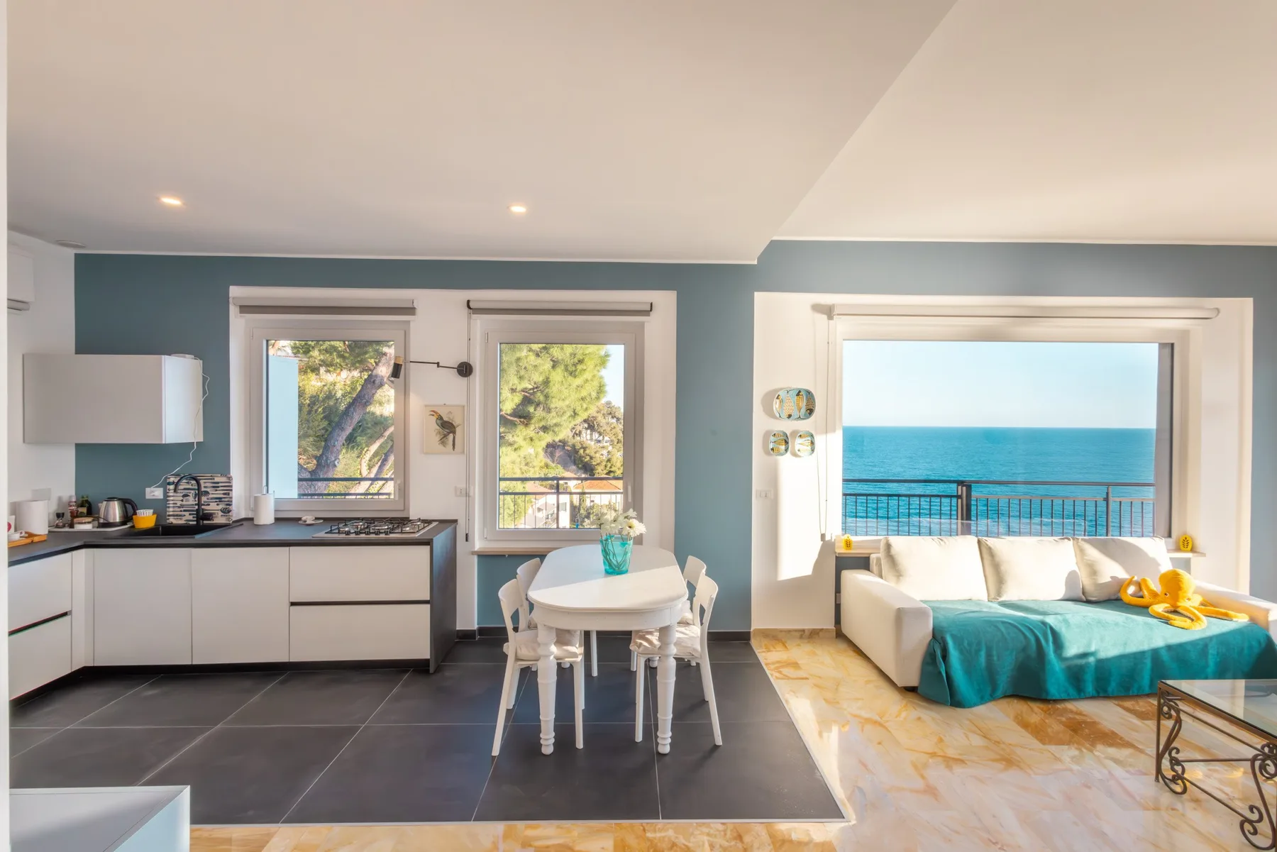 Una luminosa estancia diáfana combina cocina, mesa de comedor y asientos junto a una amplia vista al mar.