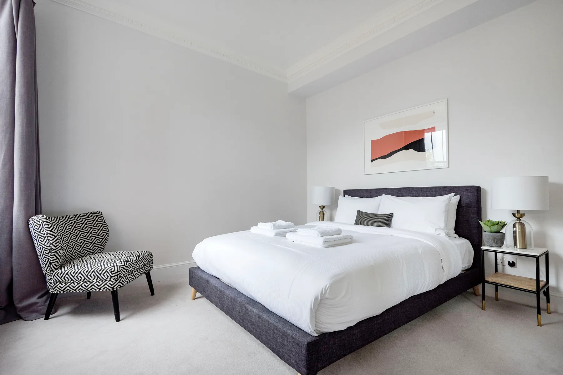 Un dormitorio luminoso con una cama bien hecha y una silla tapizada.