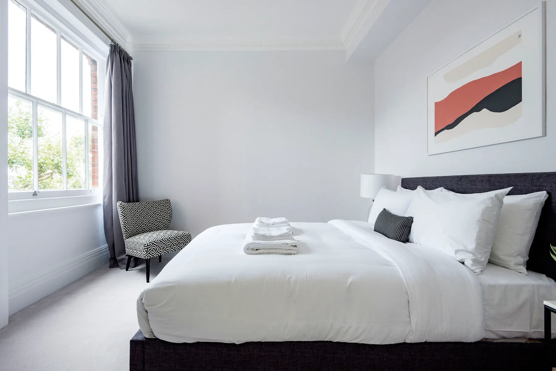 A bright bedroom with a neatly made bed and a large window.