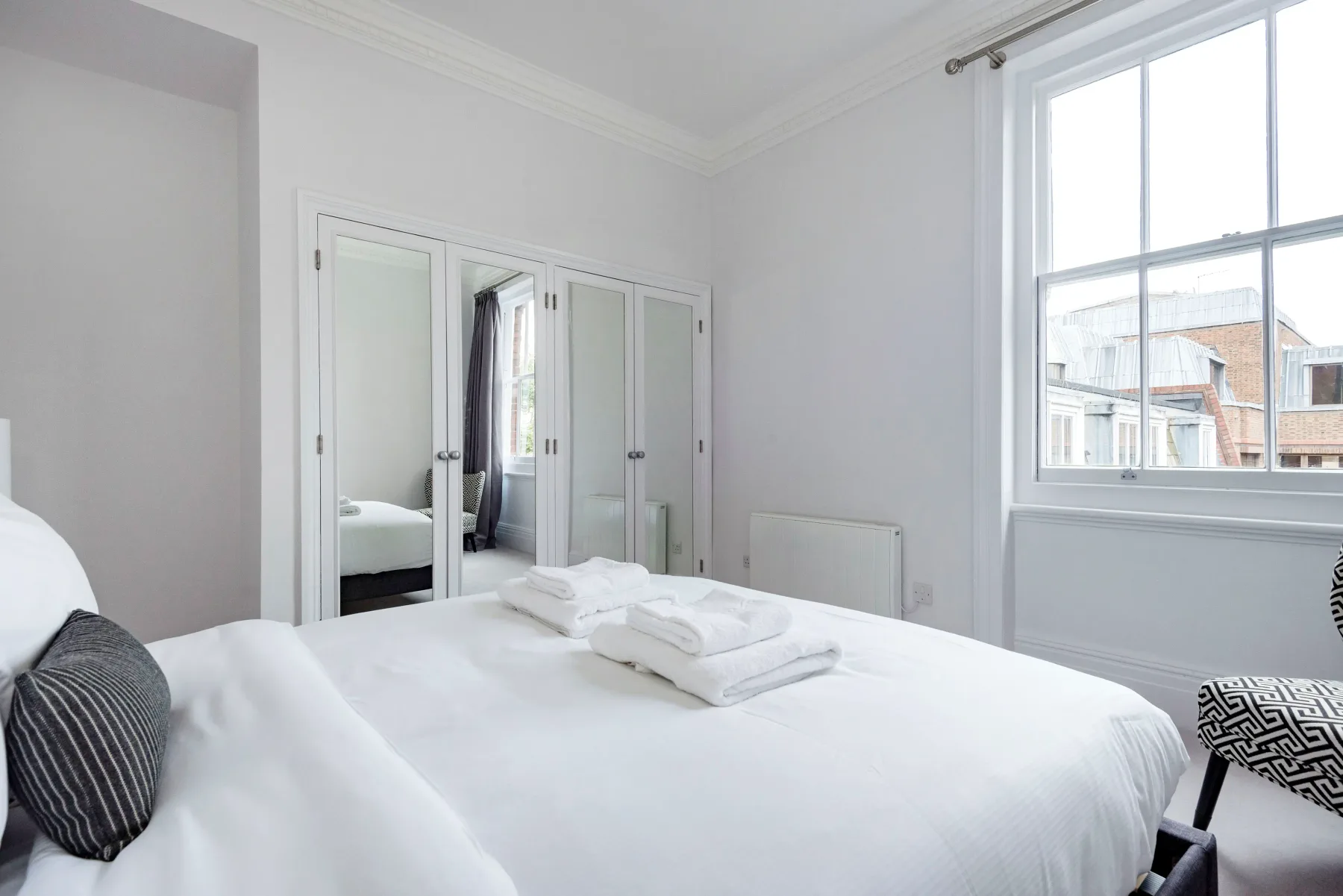 A bright bedroom with a neatly made bed and mirrored wardrobe doors.