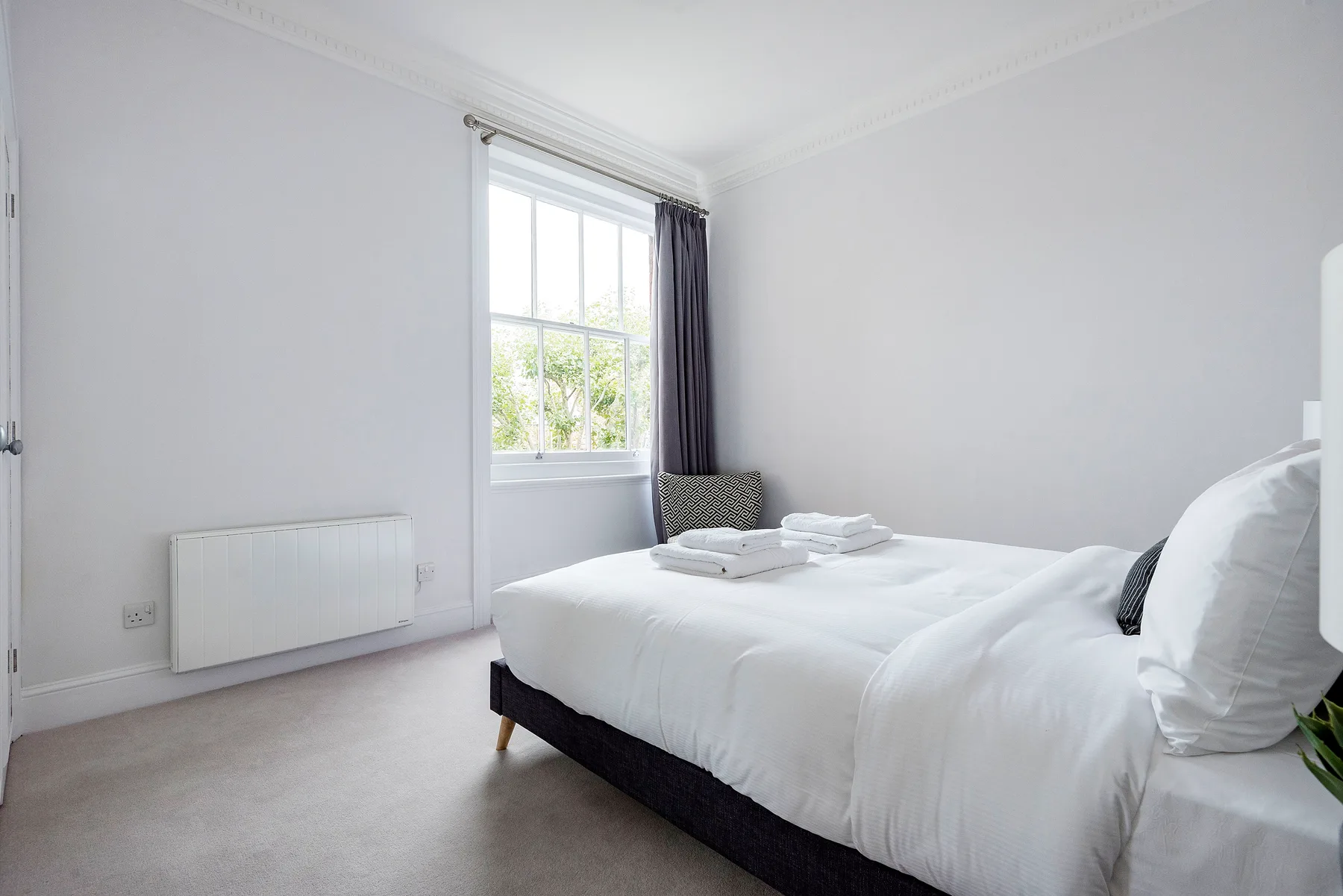 A bright bedroom with a neatly made bed beside a window.