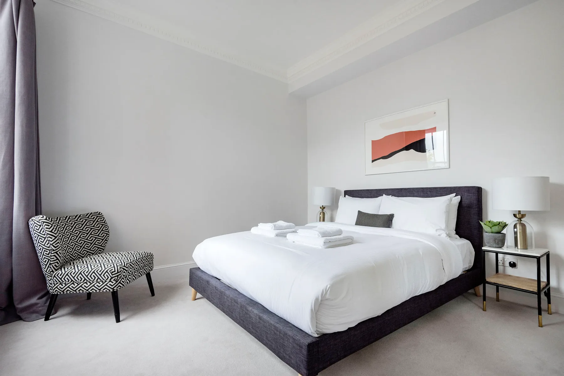 A bright bedroom with a neatly made bed and an upholstered chair.